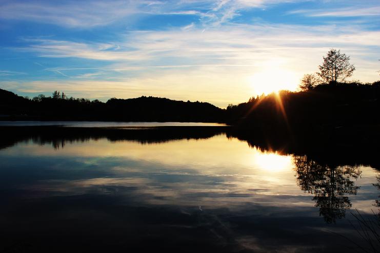 Sonnenuntergang über einem ruhigen See mit reflektierenden Bäumen und einem farbenfrohen Himmel.